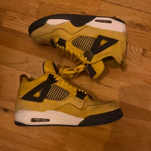 Jordan 4 Lightning - Snygga gula sneakers med svarta och vita detaljer. Skorna har snörning och en rund tå. Perfekta för dig som vill sticka ut med en färgglad stil.