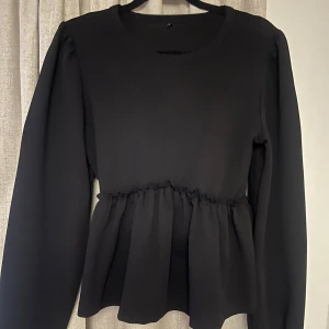 Svart långärmad topp med volang - Snygg svart topp med långa ärmar och volangdetalj i midjan. Storlek M men som en S