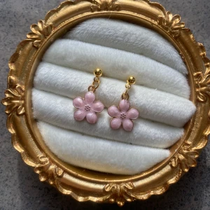 Rosa blommiga örhängen - Handgjorda Charmiga örhängen med rosa blommor och guldfärgade detaljer. Perfekta för att ge en söt och feminin touch till din outfit.