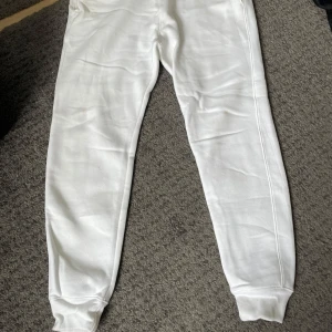 Vita mjukisbyxor från Hollister - Säljer ett par vita mjukisbyxor från Hollister. Byxorna har en bekväm passform med snörning i midjan och ribbade muddar vid bensluten. Perfekta för en avslappnad stil.