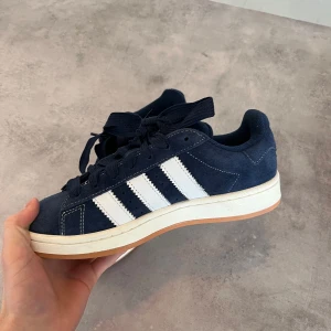 Adidas Campus sneakers i mörkblå mocka - Snygga Adidas Campus sneakers i mörkblå mocka med klassiska vita ränder och gummisula. Skick: 10/10 som nya | hör av dig vid minsta fundering! Mvh Nouk 