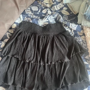 Svart volangkjol - Säljer en svart kortkjol med volanger. Kjolen har en elastisk midja som ger en bekväm passform. Perfekt för att skapa en trendig look.