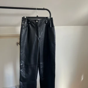 Svarta PU-byxor från NA-KD - Snygga svarta PU-byxor från NA-KD med en straight passform. Byxorna har en klassisk design med fem fickor och knappar i silverfärg. Perfekta för en stilren look.