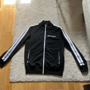 Svart träningsjacka från Palm Angels - Snygg svart träningsjacka från Palm Angels, säljes då den inte används längre. Mycket bra skick, storlek L