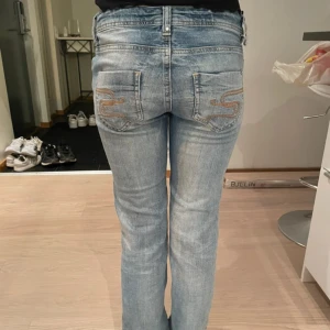 Blå jeans med broderade bakfickor - Snygga blå jeans med broderade detaljer på bakfickorna. De har en klassisk femficksdesign och en knappgylf. Midja:35cm Innerbenslängden: 82cm 