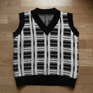 Svartvit stickad väst - Snygg svartvit stickad väst med ett rutigt mönster. Västen har en v-ringad design och är perfekt för att styla med lager på lager stil eller över en vit skjorta, sitter lite oversize för mig, skulle säga passar även 36 ? 