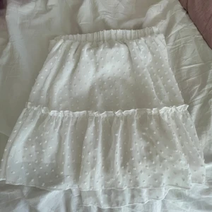 Vit prickig kjol - Söt vit kortkjol med prickigt mönster och volangdetaljer. Perfekt för en somrig look. Elastisk midja för bekväm passform.