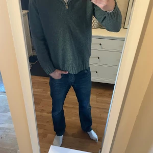 Grön stickad tröja från Dressmann - Säljer en stilren grön stickad tröja från Dressmann med dragkedja vid halsen. Perfekt för kyligare dagar med sin ribbade krage och muddar. Tröjan har långa ärmar och en klassisk passform. Hör av dig vid intresse!