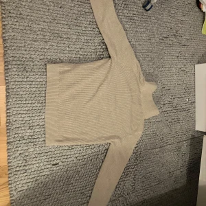 Beige ribbad tröja från East West - Säljer en stilren beige ribbad tröja från East West. Tröjan har en dragkedja vid halsen och långa ärmar, perfekt för kyligare dagar. Den är både bekväm och snygg, ett måste i garderoben!