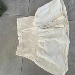 Beige stickad kjol med knytband - Säljer en söt beige stickad kjol med elastisk midja och dekorativa knytband med pärlor. Kjolen har en kort längd och är perfekt för en avslappnad stil. Passar bra till en mysig tröja eller blus.