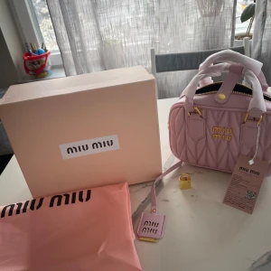 Rosa quiltad handväska från Miu Miu - Säljer en superfin rosa handväska från Miu Miu med quiltad design och gulddetaljer. Väskan har dubbla handtag och en avtagbar axelrem. Perfekt för att ge din outfit en lyxig touch! 💖