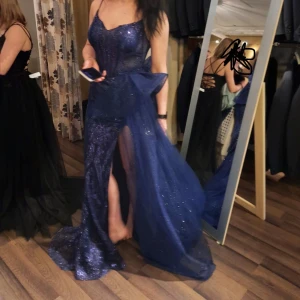 Blå glittrig långklänning - Elegant blå långklänning med glittrigt material och smala axelband. Klänningen har en slits framtill och en volangdetalj vid midjan som ger en extra touch av glamour.OBS! Volangdetaljen är avtagbar ‼️‼️