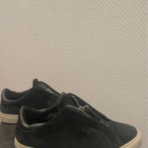 Axel arigato  - Snygga svarta axel arigato clean 90 sneakers i mocka med dragkedja framtill. Skorna har en rund tå och en vit sula som ger en cool kontrast. Perfekta för en stilren look.Påse ingår. Priset kan diskuteras. Frågor,Skriv!
