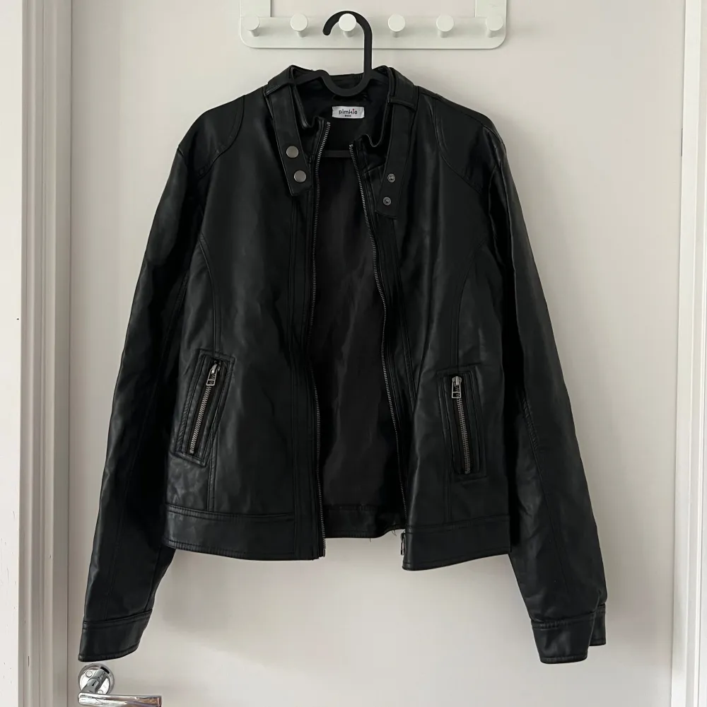Snygg svart skinnjacka från Pimkie med dragkedja och knappar. Jackan har en cool bikerstil med två dragkedjefickor framtill och detaljer vid kragen. Perfekt för att ge din outfit en edgy touch. Se baksida för skavank. Inget som man stör sig på. . Takit.