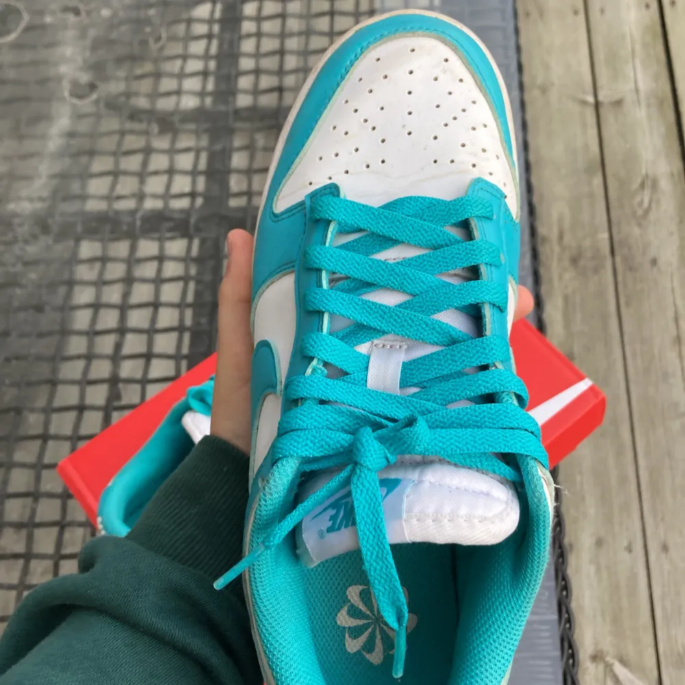 Säljer ett par snygga Nike Dunk sneakers från Footlocker i en fräsch turkos och vit färgkombination. Skorna har klassisk snörning och en rund tå. Perfekta för dig som vill ha en stilren och sportig look. Kommer i originalkartong.. Kengät.