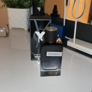 Yves Saint Laurent Eau de Parfum - Elegant parfym från Yves Saint Laurent i en stilren flaska med svart och silverdetaljer. Flaskan rymmer 100 ml och har en modern design med en tydlig logotyp. Perfekt för den som söker en sofistikerad doft. Priset kan diskuteras 