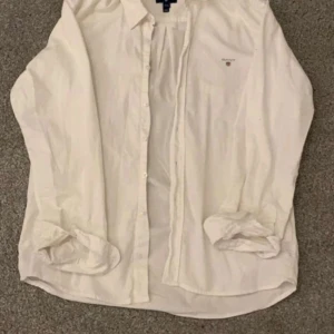 Vit skjorta från GANT - Säljer en klassisk vit skjorta från GANT. Skjortan har långa ärmar och knappar framtill. Perfekt för en stilren look.