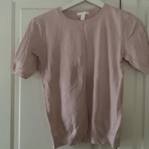 Ljusrosa kortärmad tröja från H&M - Säljer en ljusrosa kortärmad tröja från H&M Basics. Tröjan har en rund halsringning och ribbade kanter vid ärmslut och nederkant. Perfekt för en avslappnad stil.