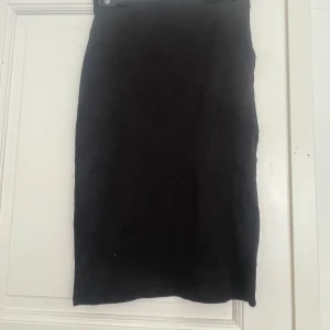 Svart knäkjol från KappAhl, stl 36 - Enkel och stilren svart knäkjol från KappAhl i storlek 36. Kjolen har rak passform och är tillverkad i ett mjukt, stretchigt material som sitter snyggt på kroppen. Perfekt att matcha med en crop top eller stickad tröja.