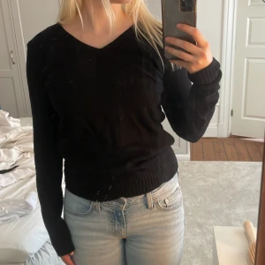 Svart stickad tröja från Vila - Svart v-ringad tröja från Vila med lång ärm och ribbade muddar vid ärmslut och nederkant. Enkel och stilren modell som passar perfekt till jeans eller kjol. Mjuk och skön, tillverkad i bomullsmix.