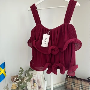 Vinröd volangtopp från NA-KD - Superfin vinröd topp från NA-KD med breda axelband och plisserat tyg. Toppen har flera volanger. Helt ny med prislapp.