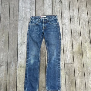 Levi's 511 blå jeans straight fit - Säljer ett par klassiska Levi's 511 jeans i blå tvätt med snyggt slitna detaljer. Modellen har rak passform, fem fickor och normal midja. Jeansen är gjorda i robust denim och har den ikoniska röda Levi's-taggen bak. Perfekta för en avslappnad och stilren look.