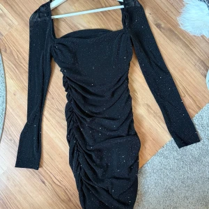 Svart glittrig klänning  - Supersnygg svart glittrig miniklänning från Kiss The Sky (Köpt på Nelly). Klänningen har långa ärmar, rynkade detaljer längs sidorna och en fyrkantig urringning. Materialet är stretchigt. Passar verkligen perfekt till en utekväll ❤️ strl L 