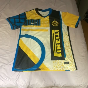 Inter Milan Nike fotbollströja blå/gul - Inter Milan matchtröja från Nike med unikt grafiskt mönster i blått, gult, svart och vitt. Tröjan har korta ärmar, V-ringning och stora tryck med Pirelli-logga och klubbmärke på bröstet. Tillverkad i lätt och ventilerande polyester för maximal komfort.