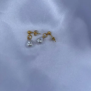 Guldörhängen med droppformade pärlor - Snygga örhängen med guldfärgade stift och droppformade vita pärlor som hänger ner. Perfekta för att ge en elegant touch till din look. Klassisk design som passar till många stilar.