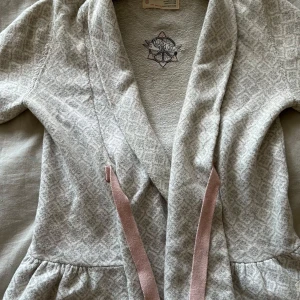 Grå Odd Molly kofta - Superfin ljusgrå kofta från Odd Molly med diskret mönster och rosa knytband. Koftan har omlottmodell, långa ärmar och broderad logga på insidan. Många fina detaljer och jätteskönt material💕