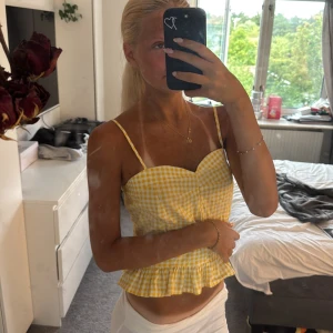 Gul rutig croppad topp Gina Tricot - Superfin gul och vit rutig croppad topp från Gina Tricot med smala axelband, söt volangkant nertill och hjärtformad urringning. Toppen har dragkedja i ryggen och är perfekt för sommarens alla tillfällen. Säljer då den är lite för stor på mig🥰