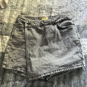Gråa kjolshorts i jeans från JJXX - Snygga gråa kjolshorts i jeans från JJXX med hög midja och klassisk femficksdesign. Shortsen har bälteshällor, knapp- och dragkedjestängning samt raka ben. Perfekta för sommardagar och ger en cool vintagekänsla till din outfit. Helt ny använd endast 1 gång!