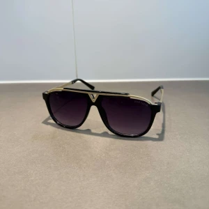 Lv glasögon  - Snygga solglasögon från Louis Vuitton med svart båge och guldiga detaljer. Pilotformade glas med mörka tonade linser och diskret logga på sidan. Riktigt lyxig vibe och perfekt accessoar för att sticka ut.