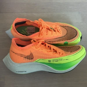 Nike ZoomX Vaporfly Next% 2 Orange - Nike ZoomX Vaporfly Next% 2 i neonorange och grönt med svart swoosh. Lätta löparskor med ventilerande mesh, snörning och responsiv ZoomX-sula. Perfekta för dig som vill maxa din löpning med stil och teknik.