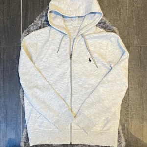 Ralph Lauren Zip Hoodie Grå - Stilren och klassisk grå zip-hoodie från Ralph Lauren, storlek M.  Hoodien är i mycket fint skick, endast sparsamt använd. Perfekt till både vardags och avslappnad layering.   Sökord: , college-
