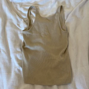 Beige guld glittrig ribbad linnetopp från & Other Stories - Supersnygg beige ribbad linnetopp från & Other Stories. Toppen har smala axelband, croppad passform och ett diskret glittrigt skimmer i tyget. Perfekt att styla med jeans eller kjol för en trendig look.