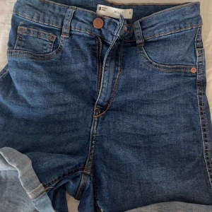 Blå jeans Molly från Gina Tricot - Säljer ett par klassiska blå jeans från Gina Tricot, modell Molly. Jeansen har fem fickor, dragkedja och knapp framtill samt snygga kontrastsömmar. Perfekt passform och tidlös stil som funkar till allt.