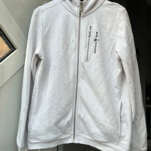 Vit zipjacka från Sail Racing - Vit jacka med dragkedja från Sail Racing. Jackan har huva, bröstficka med dragkedja och två sidofickor. Broderad logga på bröstet. Tillverkad i mjuk bomull, perfekt för chill dagar. Långärmad och stilren design som funkar till det mesta. Har lite små sminkfläckar, kanske försvinner i tvätten men vet ej! Skriv för fler och närmare bilder, pga de små fläckarna och att jag vill få den sålt snabbt så ett lågt pris🥰🥰nypris ca 1100kr, tröjan är i stl 174 men passar mig super som har s/m❤️