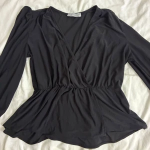 Svart omlottblus från Paul Mark - Svart omlottblus från Paul Mark med v-ringning och långa ärmar. Blusen har resår i midjan som ger en snygg siluett och ett flowigt fall. Sitter som storlek S-XS. Köpt från Paul Mark utomlands finns inte i Sverige. 