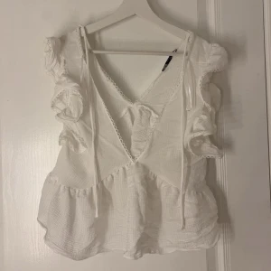 Vit volangblus från Zara - Supersöt vit blus från Zara med volanger på axlarna, v-ringning och knytning bak. Storlek S. Nästan aldrig använd💗