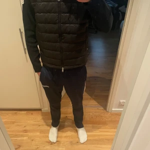 Svart moncler cardigan - Säljer en svart dunväst från Moncler med quiltad framsida och avtagbar huva. Västen har dragkedja framtill och klassisk Moncler-logga på axeln. Strl M men skulle säga att den passar bättre som Strl S, 170-175cm