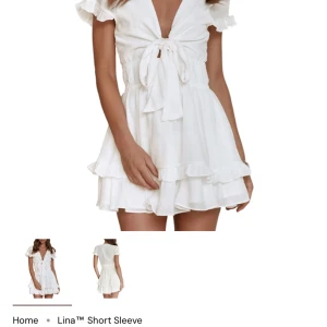 Student klänning  - Supersöt vit kort klänning från dressy med volanger, knyt framtill och smock i midjan. Klänningen har korta ärmar med volangkant och är tillverkad i 100% polyester. Perfekt för sommarens alla tillfällen! Frakt tillkommer 