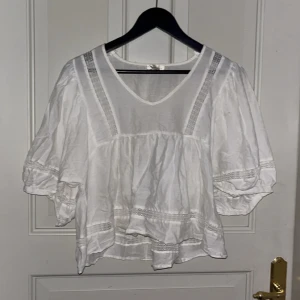 Vit blus från Angelology - Superfin vit blus från Angelology med v-ringning och vida trekvartsärmar. Blusen har snygga spetsdetaljer längs ärmar och framstycke samt en luftig, flowy passform. Perfekt för dig som gillar romantisk och bohemisk stil.