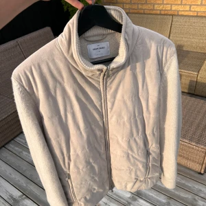 Beige stickad cardigan från Gran Sasso - Beige cardigan från Gran Sasso med quiltad framsida och stickade ärmar. Jackan har hög krage, dragkedja framtill och två fickor med dragkedja. Materialmix av ull och mocka ger en soft och clean look. Perfekt för dig som gillar stilren och avslappnad vibe. Cardiganen har några föses som syns på bilderna, främst är den lite skadad inuti!