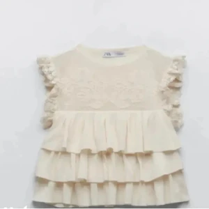 Volangblus i spets från Zara - Kollar intresset på denna supersöta ljusbeigea blus från Zara med volanger och spetsdetaljer. Ärmlös modell med volangprydda axlar och flera lager volanger nedtill. Perfekt till finare tillfällen men även till vardags! Slutsåld på hemsidan💗