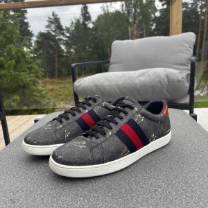 Gucci sneakers - Säljer ett par Gucci sneakers i mörkgrått med klassiskt GG-mönster, röda och blå ränder på sidorna samt olika färg på hälen – en röd och en blå. Skorna har vit platt sula och svarta skosnören. Perfekt för dig som vill sticka ut med lyxig stil. Inga defekter och nypris ligger på 9000. Priset är inte hugget i sten så hör av dig!!😆