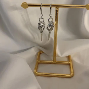 Silvriga örhängen med unik design - Säljer ett par coola silvriga örhängen med hängande detaljer som påminner om fågelkranier. De har en edgy och konstnärlig vibe, perfekta för dig som vill sticka ut. Passar till både streetwear och mer alternativa stilar.