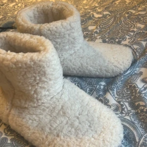 Vita fluffiga mystofflor storlek 40-41 - Supermysiga vita tofflor i fluffig polyester, perfekta för kalla dagar. De har en högre modell som går upp över ankeln och är helt täckta i mjukt teddytyg, jättesköna, köpta från Kappahl, aldrig använda 