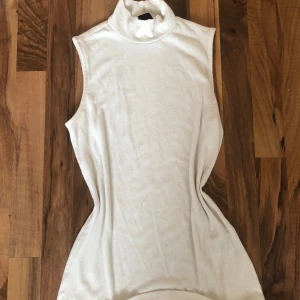 Vit polotopp Gina Tricot - Vit ribbad polotopp från Gina Tricot i ärmlös modell. Toppens höga krage ger en clean och stilren look, perfekt att matcha med jeans eller kjol. Mjuk och stretchig känsla som sitter snyggt på kroppen.