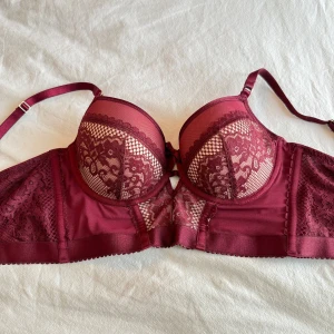 Vinröd spetsig korsett-bh - Snygg vinröd korsett-bh från Hunkemöller med ovadderade kupor och detaljerad spets framtill. Axelbanden är justerbara och tyget har en mix av mesh och spets för en extra cool look.  Har använt den enstaka gånger men tyckt att den var ganska stor för mig. Jag tvättar och skickar! Har klippt bort lappen så kommer inte ihåg storleken så jag gissar på 80C